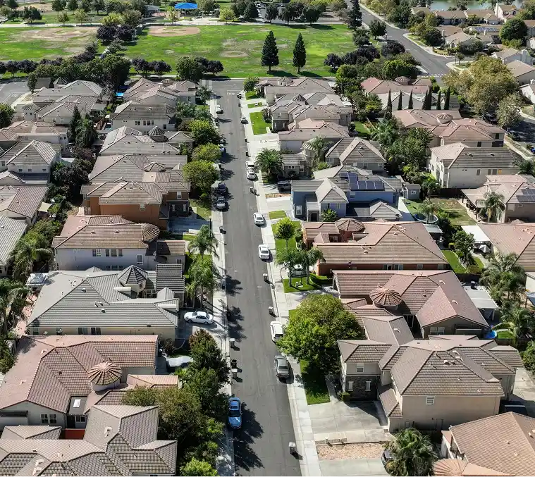 Consulting 1 Aerial view of a suburban neighborhood with tree-lined streets, rows of houses with tan roofs, and parked cars. A lush green park is visible in the distance-Homebuyer-Wallet-by-Kameron-Kang